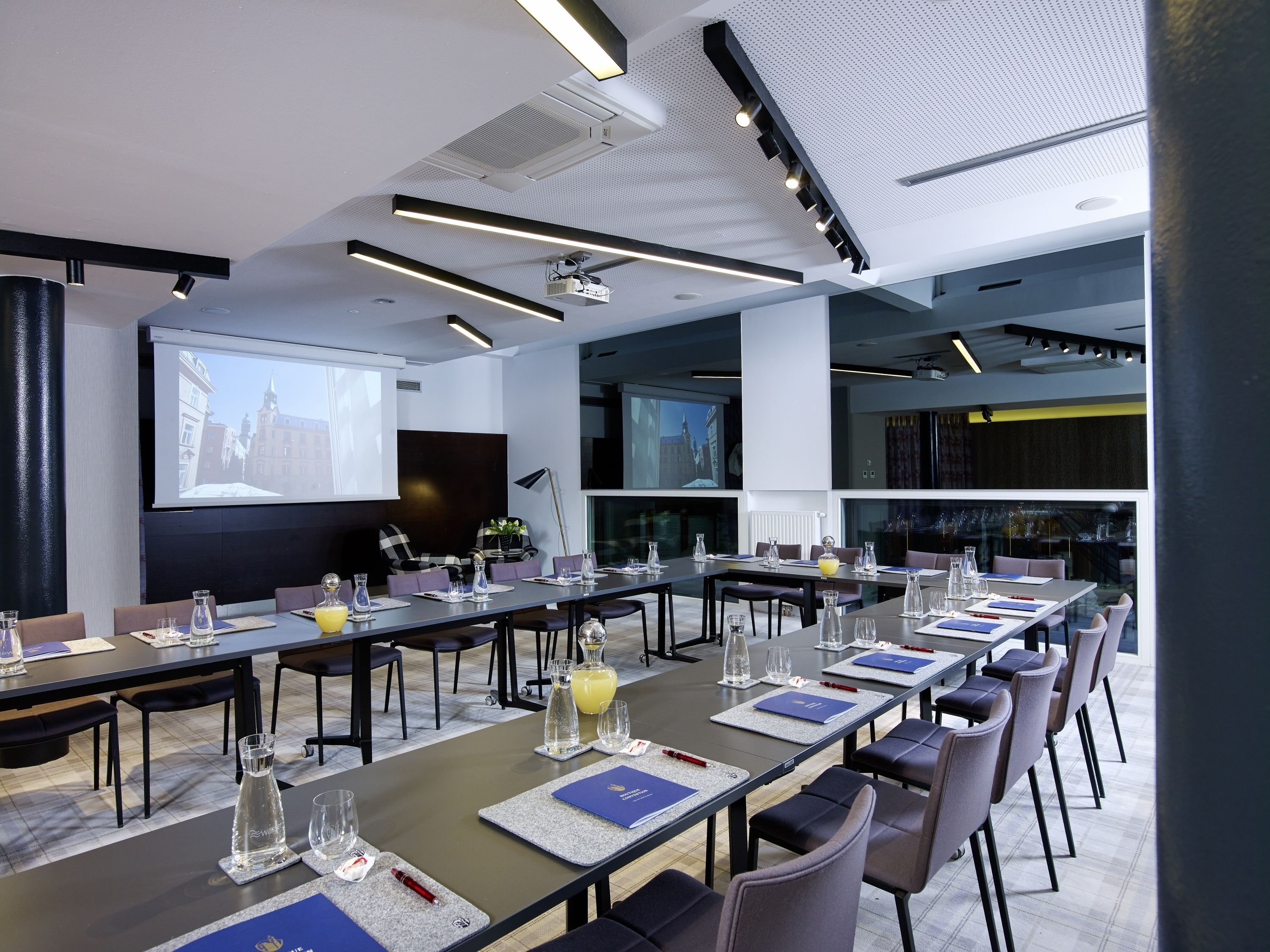 A modern conference room with long tables, chairs, and a large screen for presentations.