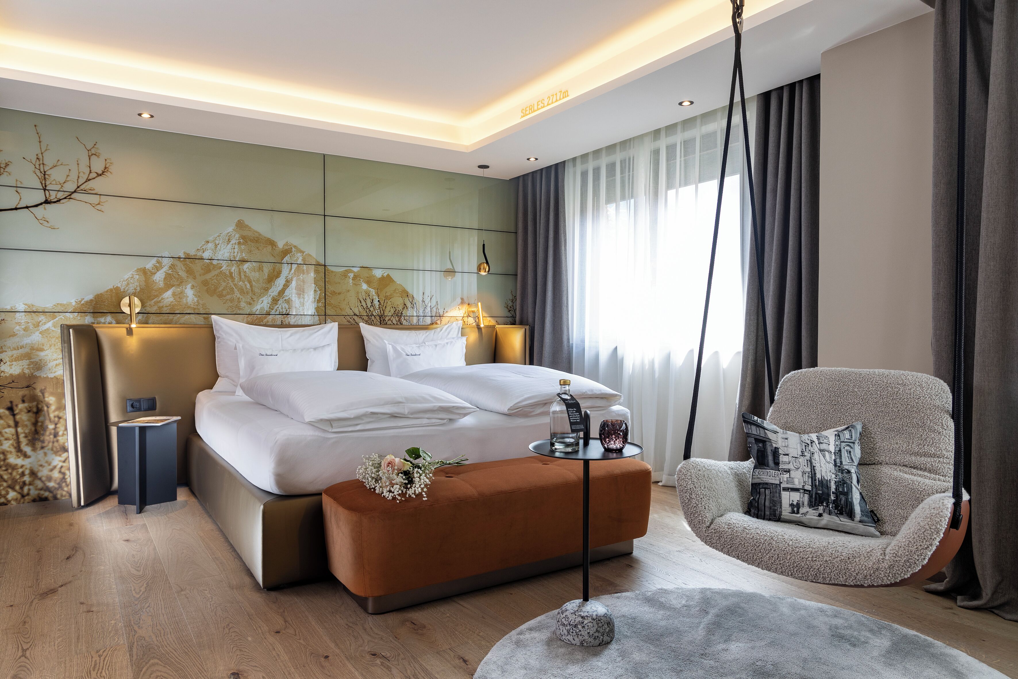 A modern hotel room with a bed, a side table, a chair, and a large window with curtains.