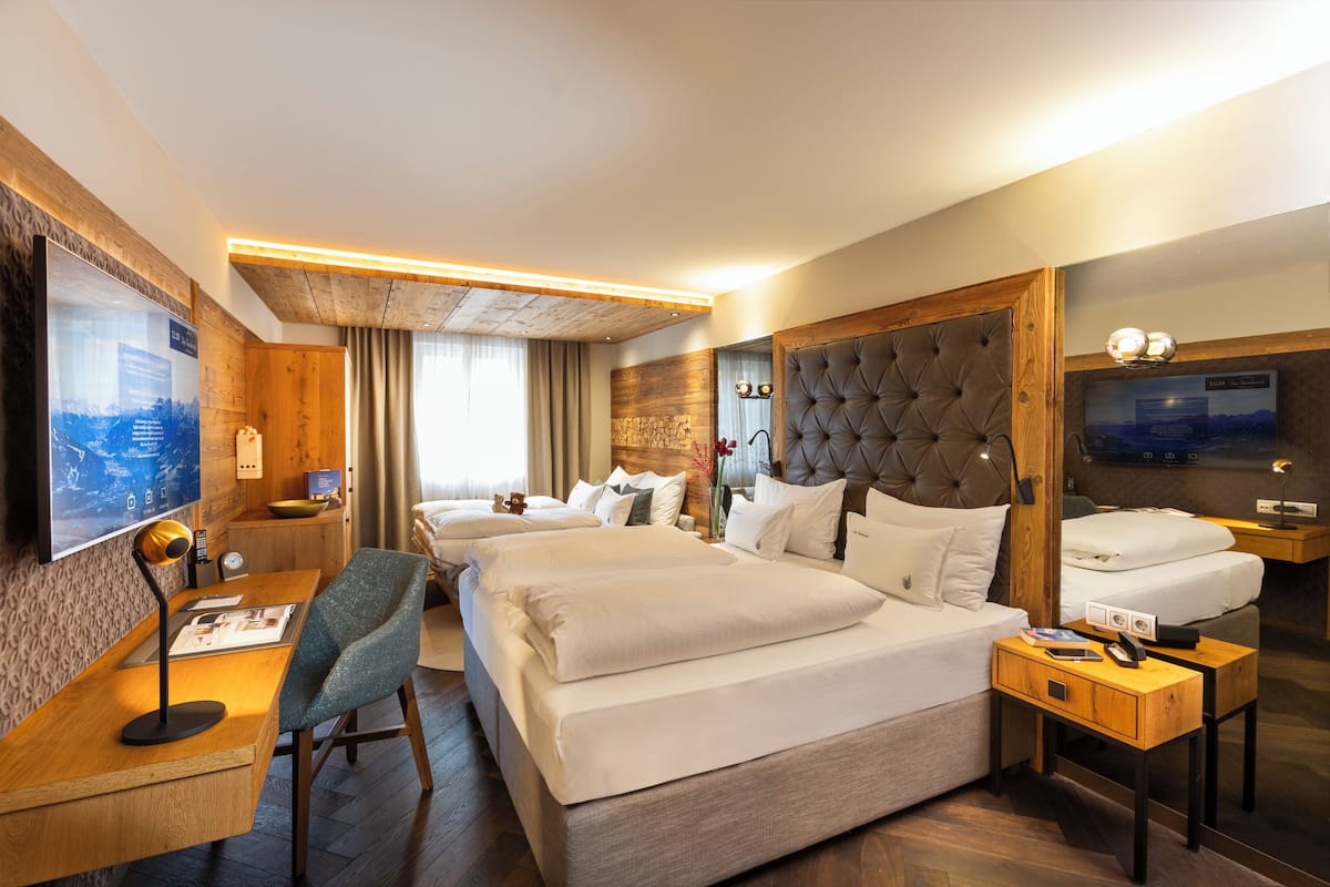 Quarto de hotel com uma cama grande, uma escrivaninha com cadeira, uma televisão e uma parede de destaque em madeira.