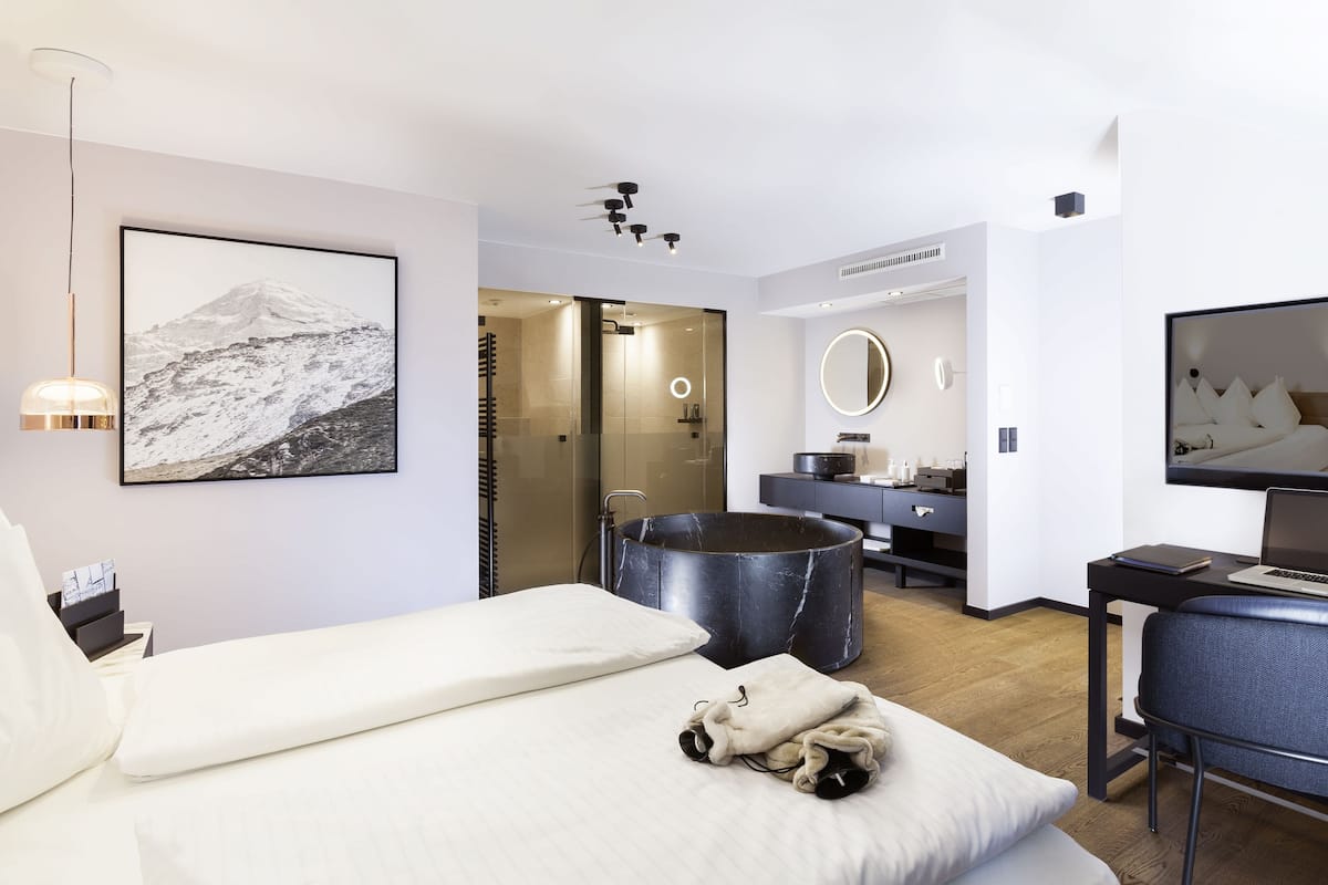 Quarto de hotel moderno com cama, escrivaninha, espelho grande e sauna.