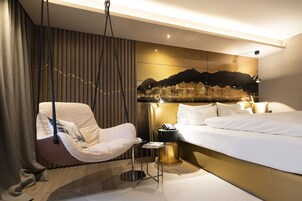 Una habitación de hotel moderna con una cama grande, una silla colgante, una mesita de noche y un televisor montado en la pared.
