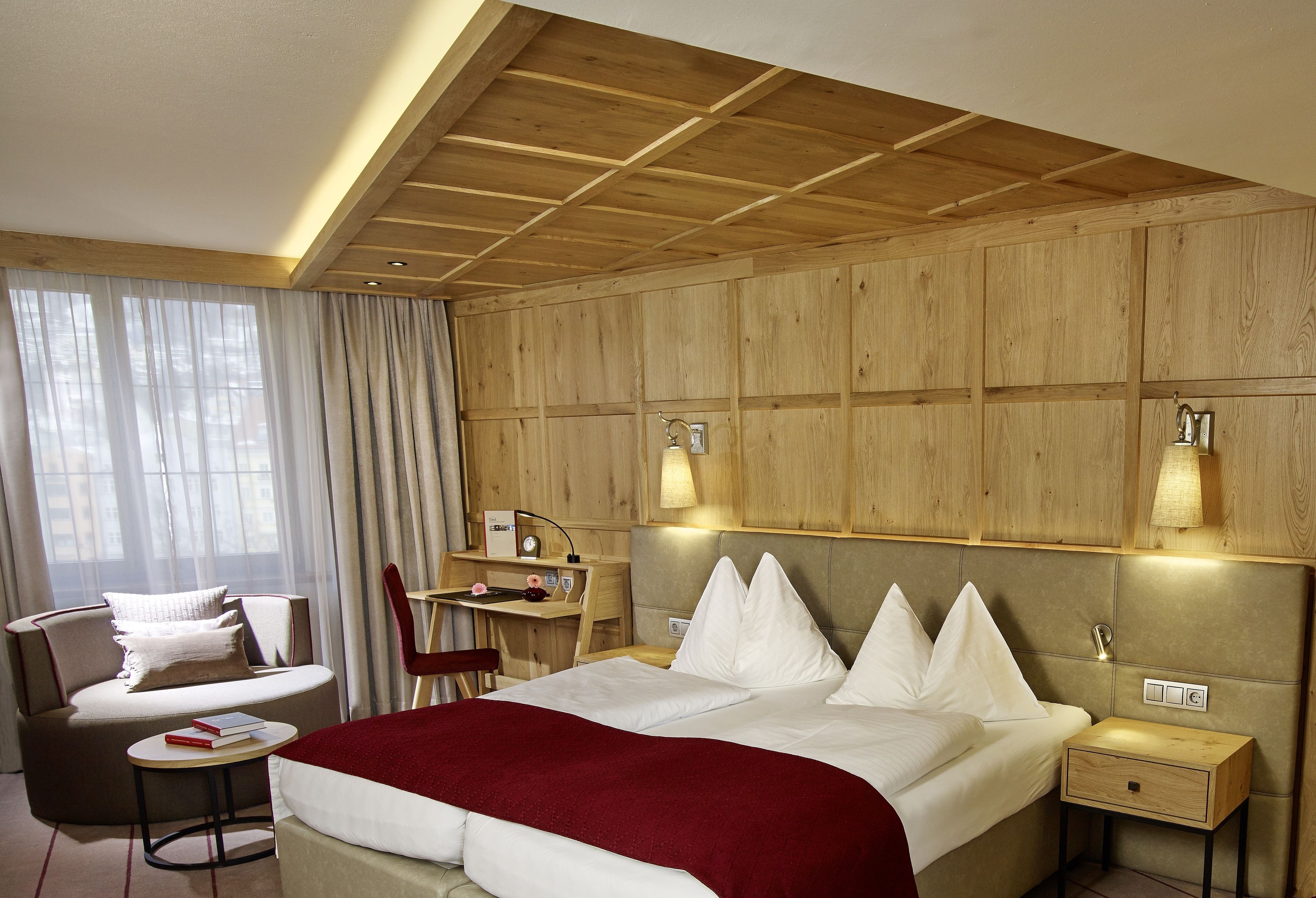 A hotel room with a large bed, a desk, a chair, and a small table.