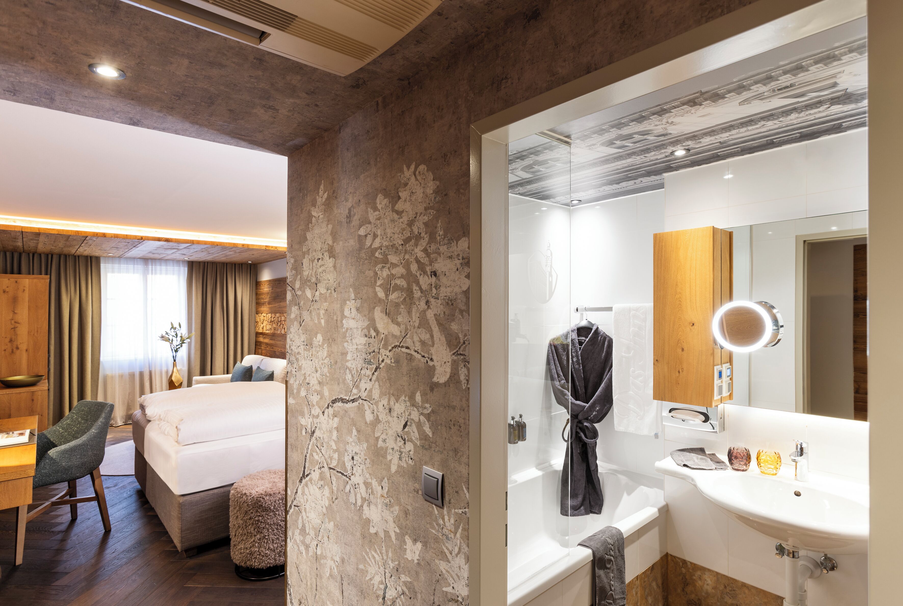 A hotel room with a bed, a desk, a chair, a bathroom with a sink, mirror, and a bathtub.
