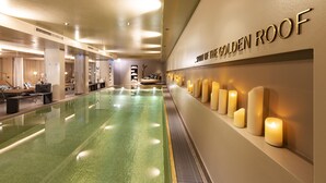Un área de piscina interior amplia, con piso verde, una pared con el texto "SPIRIT OF THE GOLDEN ROOF" y varias velas encendidas.