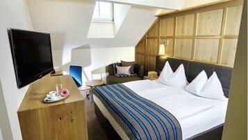A modern hotel room with a large bed, a flat-screen TV, a wooden desk, and a small table with a tray.
