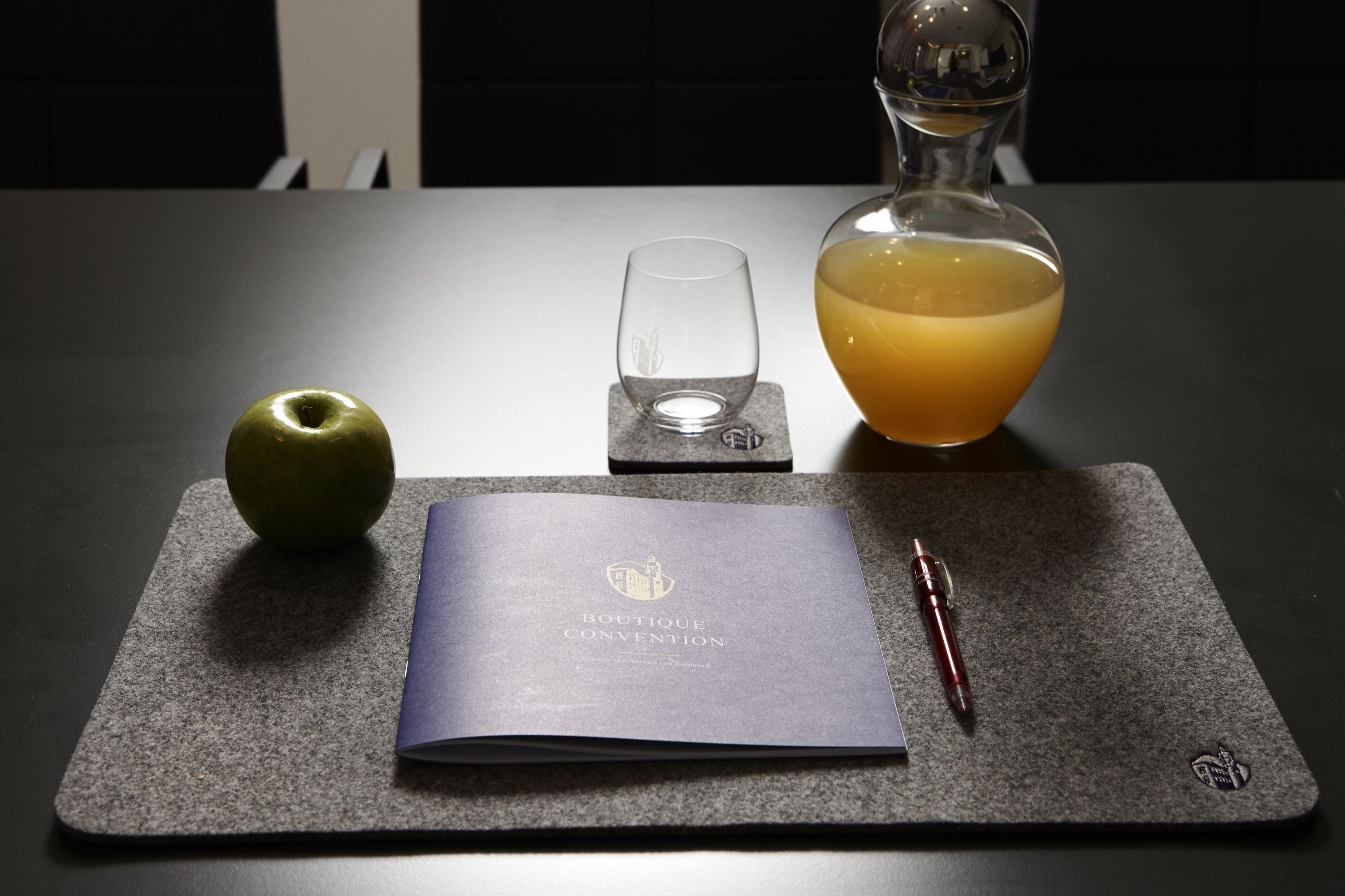 A table with a notebook, a pen, a glass, and a bottle of orange juice.