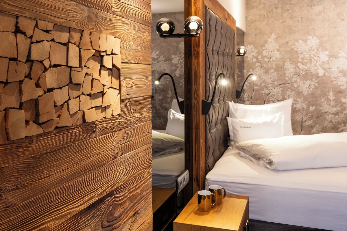 Quarto com parede de madeira, cama com roupa de cama branca e mesa de cabeceira com duas canecas.