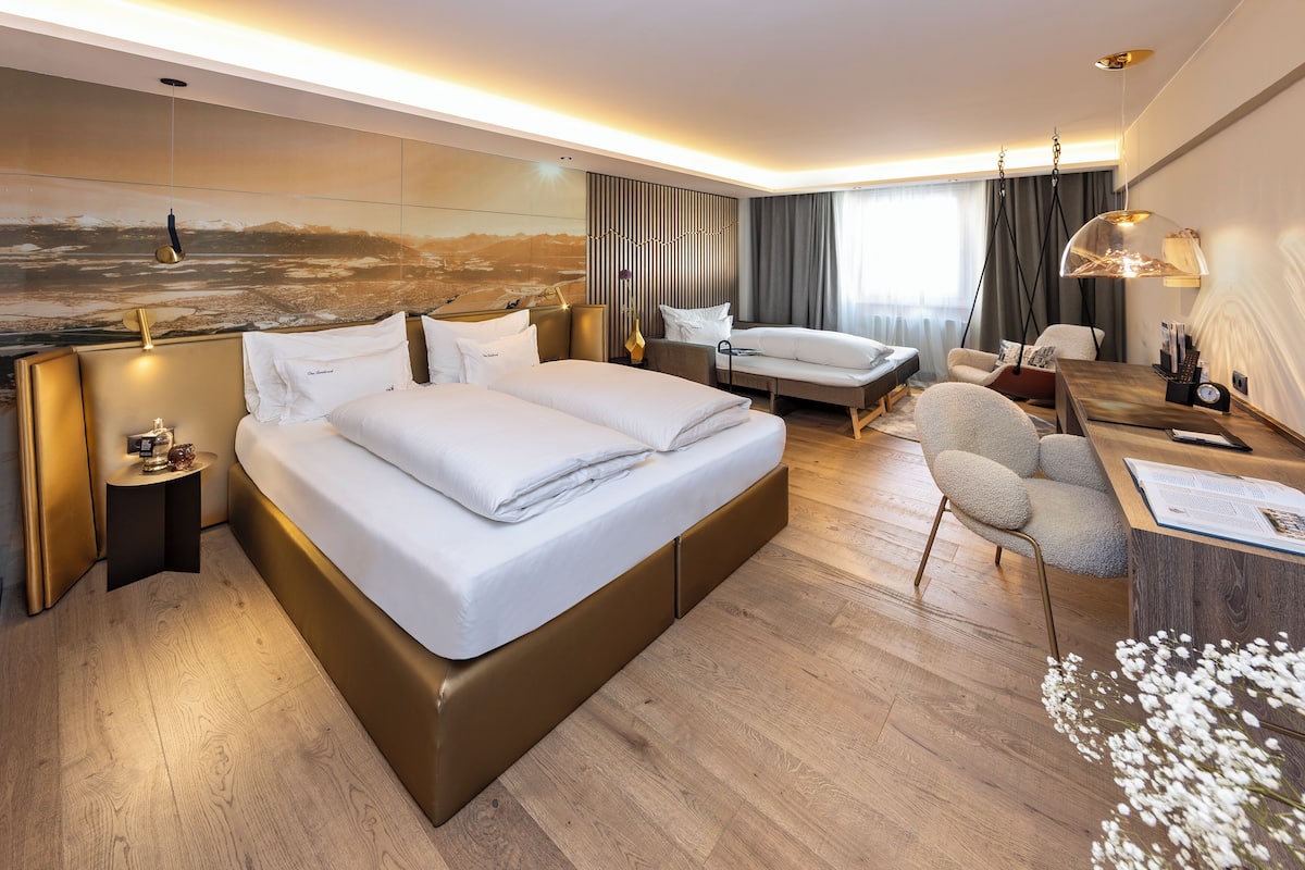 Quarto de hotel moderno com uma cama grande, uma escrivaninha, uma cadeira e vista para o horizonte da cidade.