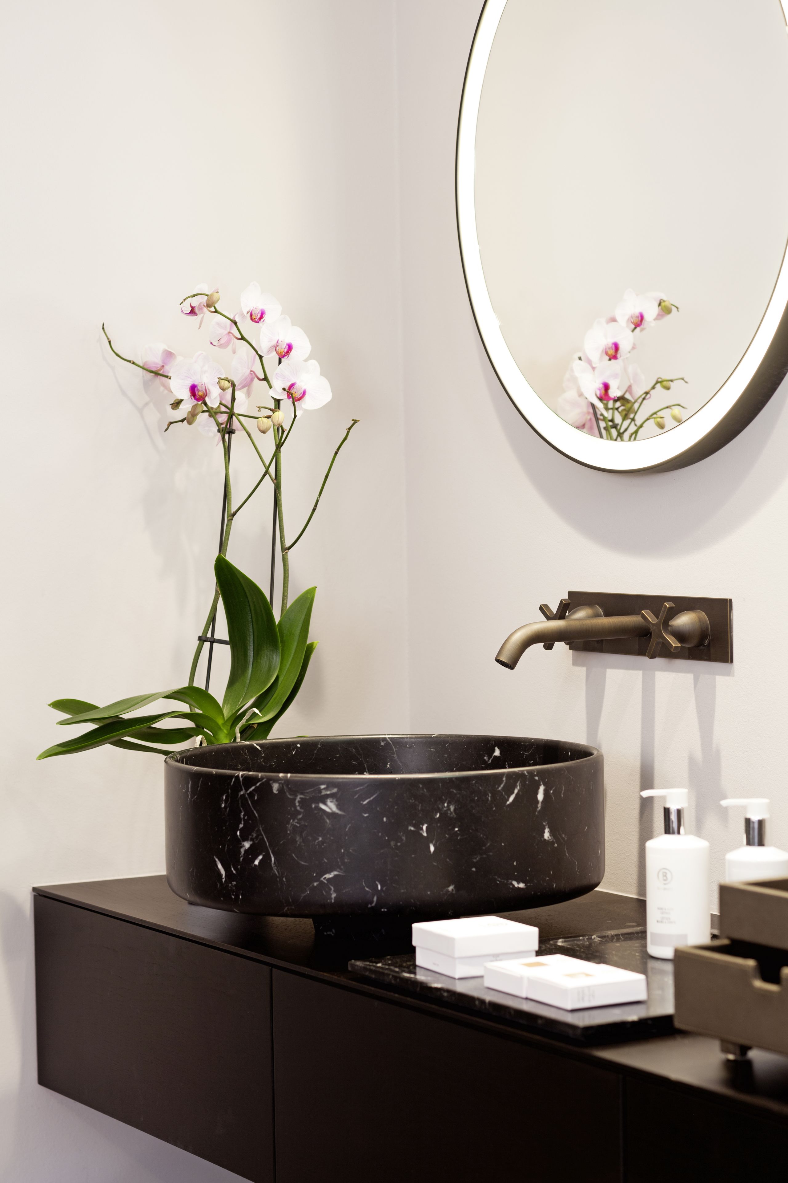 A bathroom with a black marble sink, a potted orchid, and a round mirror.