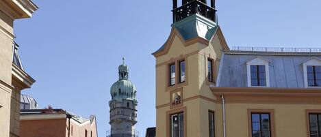 A narrow street with buildings on either side, a clock tower, and a church spire in the background.