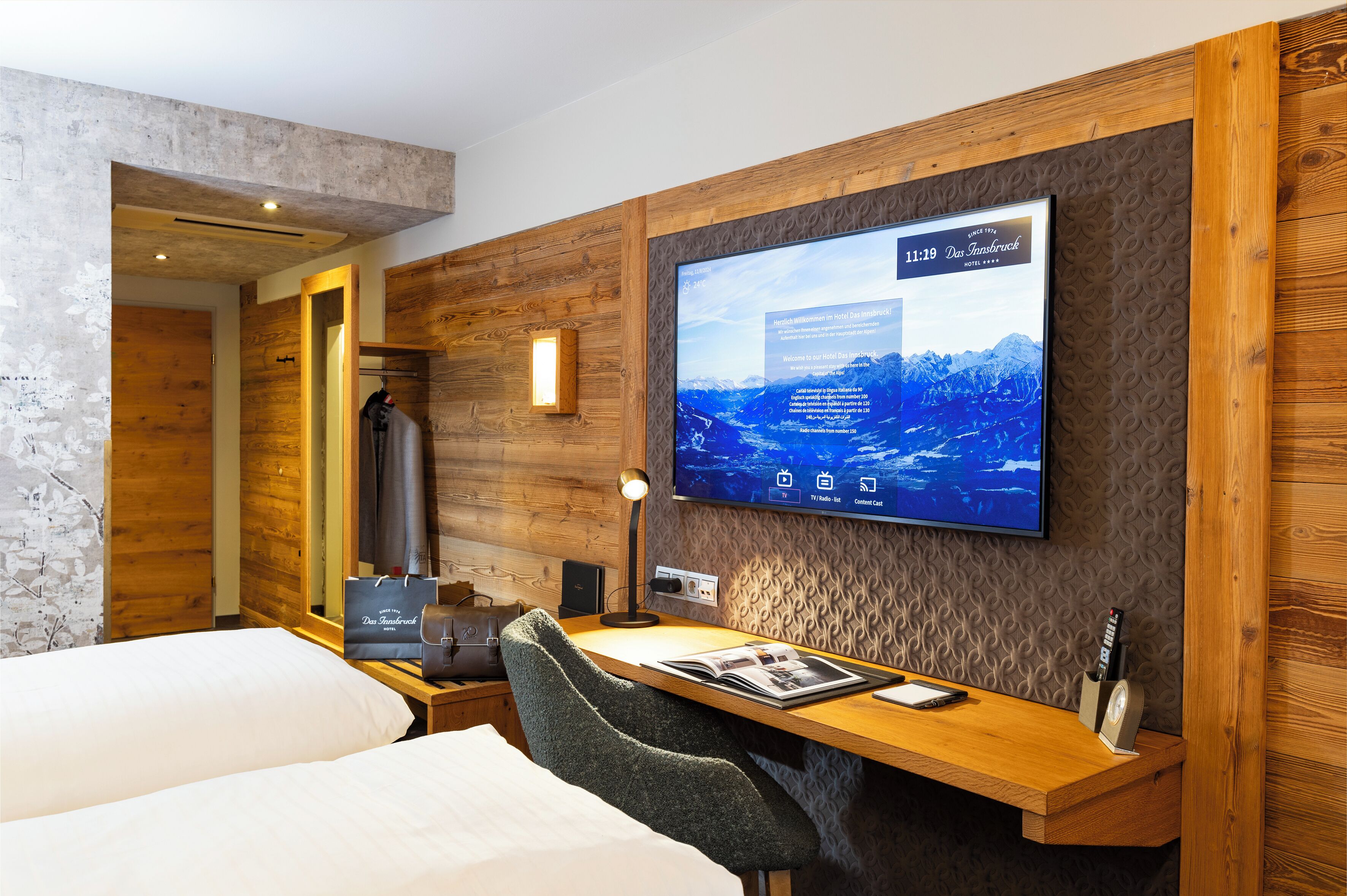 Et hotelværelse med trævæg, et fladskærms-tv, et skrivebord med stol og en seng.