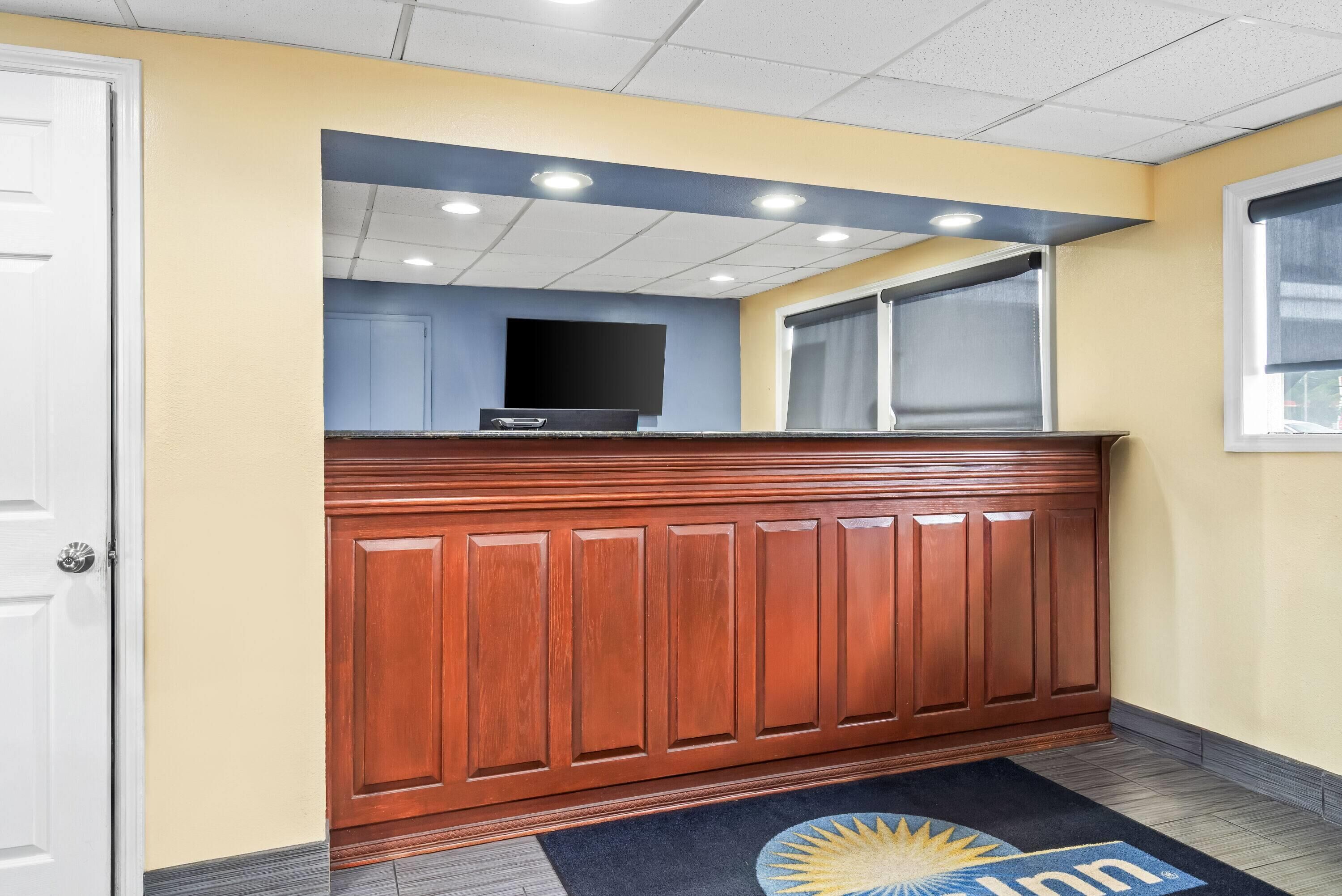 A reception area with a wooden reception desk, a flat-screen TV, and a window with blinds.