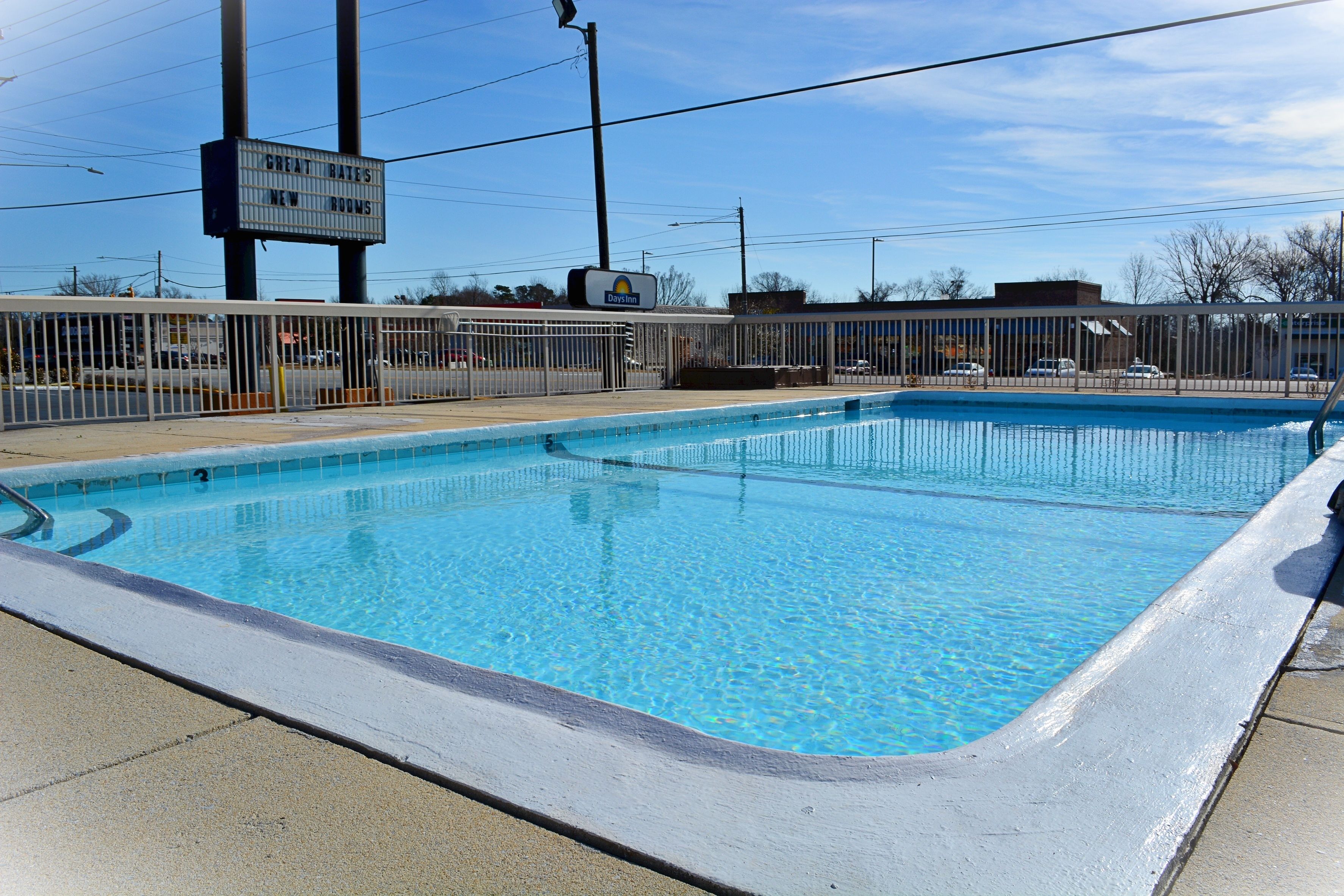 A swimming pool with a fence, a sign for Great Bates New Rooms, and a Day Inn sign in the background.