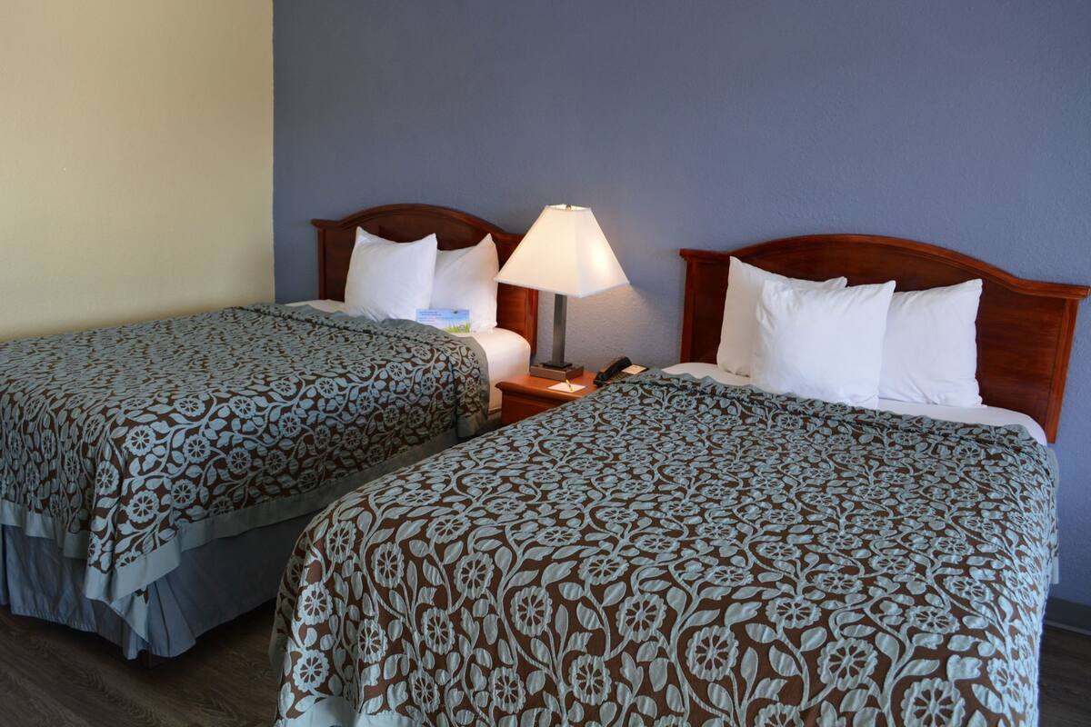 Ein Hotelzimmer mit zwei Betten, jeweils mit einem blumigen Überwurf, einer Nachttischlampe und einem Nachttisch mit Telefon.