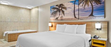 A hotel room with a large bed, a wooden headboard, a painting of palm trees, a bathtub, and a nightstand with a lamp.