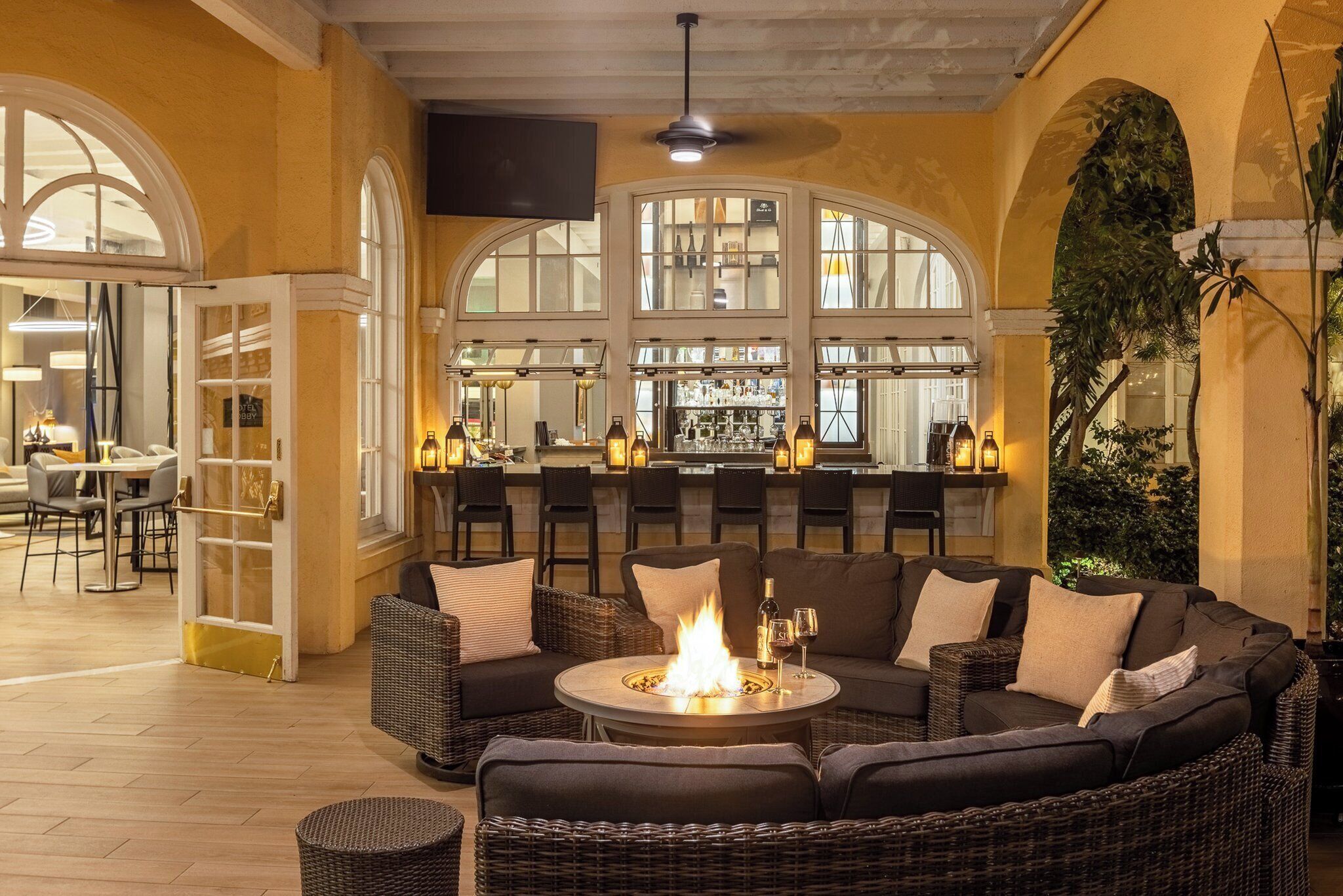 A cozy outdoor seating area with a fire pit, wicker furniture, and a bar with a view of the interior.