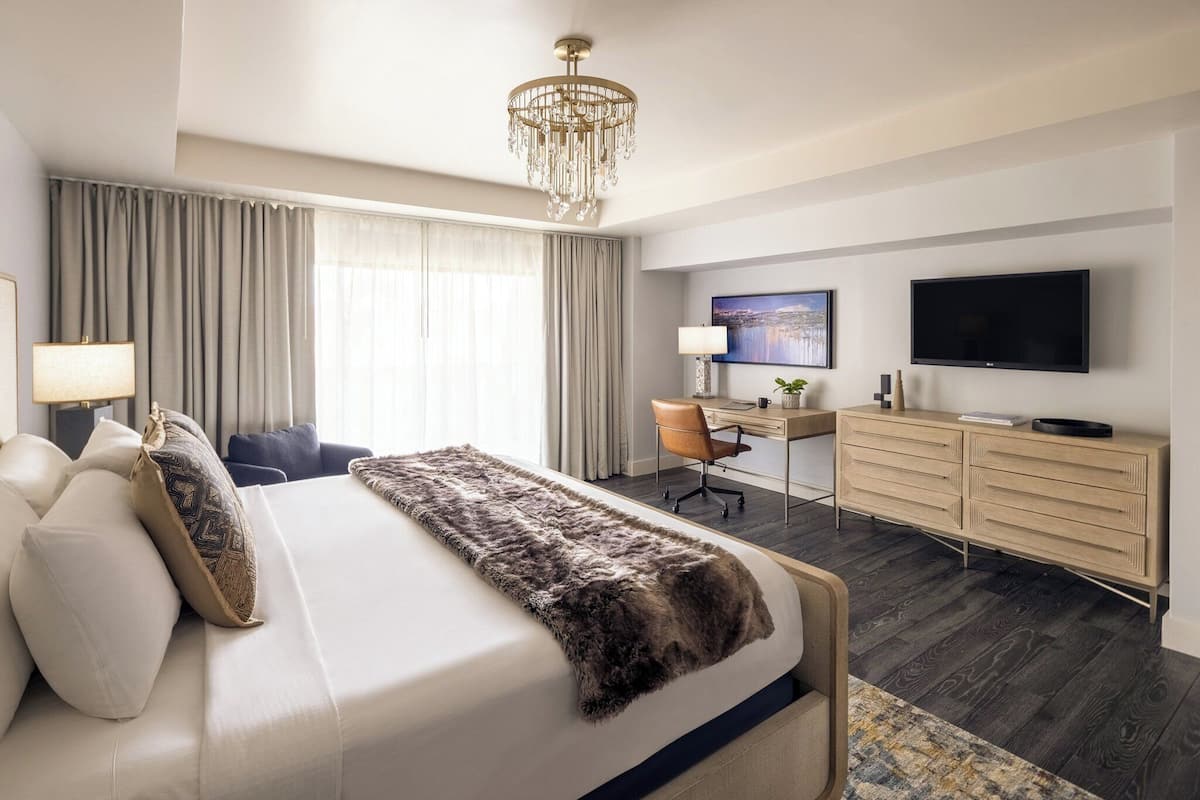 Una habitación de hotel moderna con una cama grande, un escritorio, un televisor y una araña.