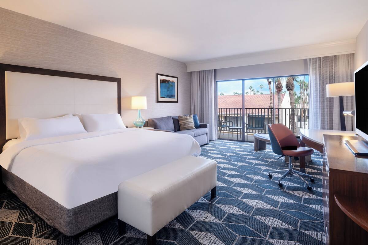 Habitación de hotel con una cama grande, un sofá, un escritorio y un balcón con vistas.