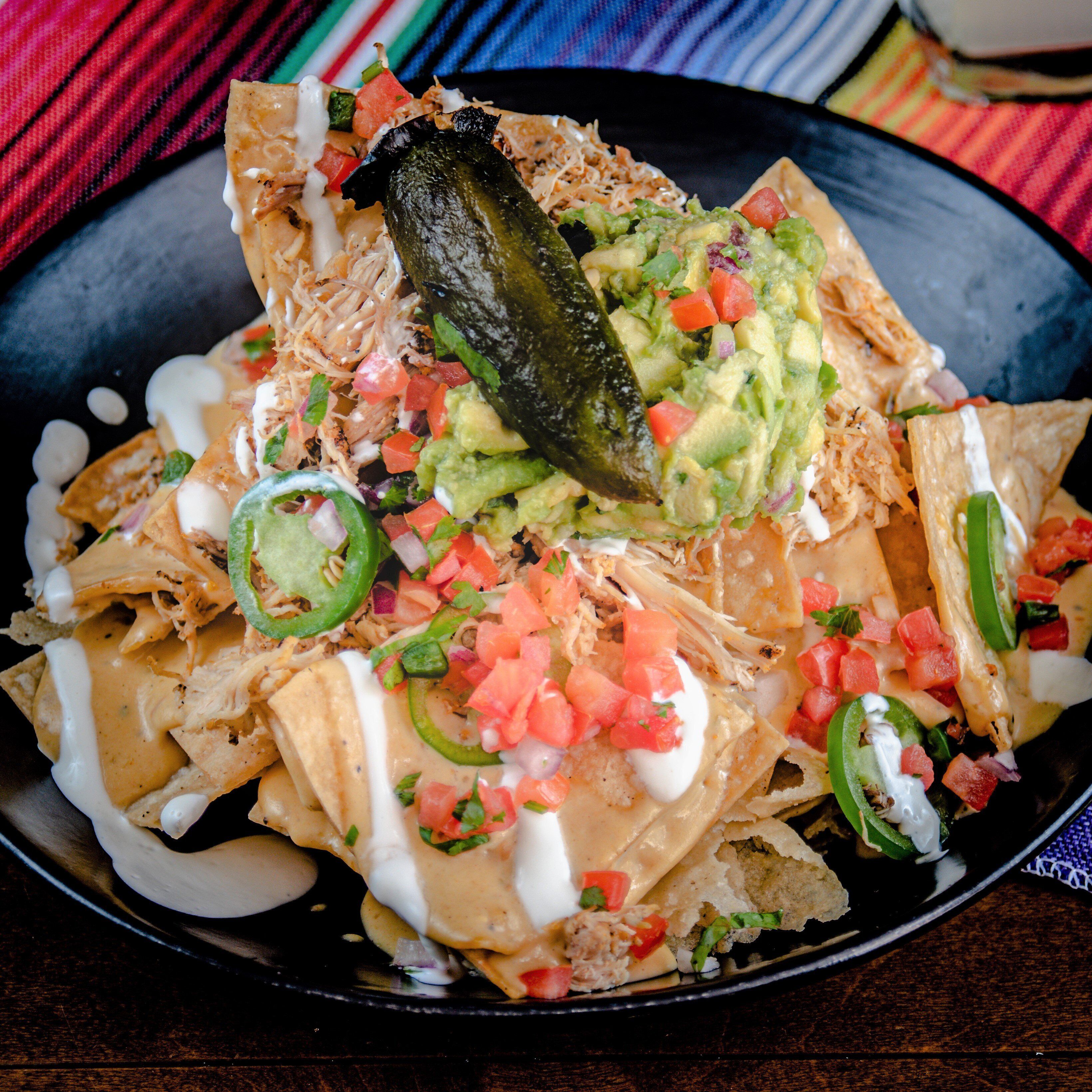 Nachos topped with shredded chicken, guacamole, diced tomatoes, and jalapeños.