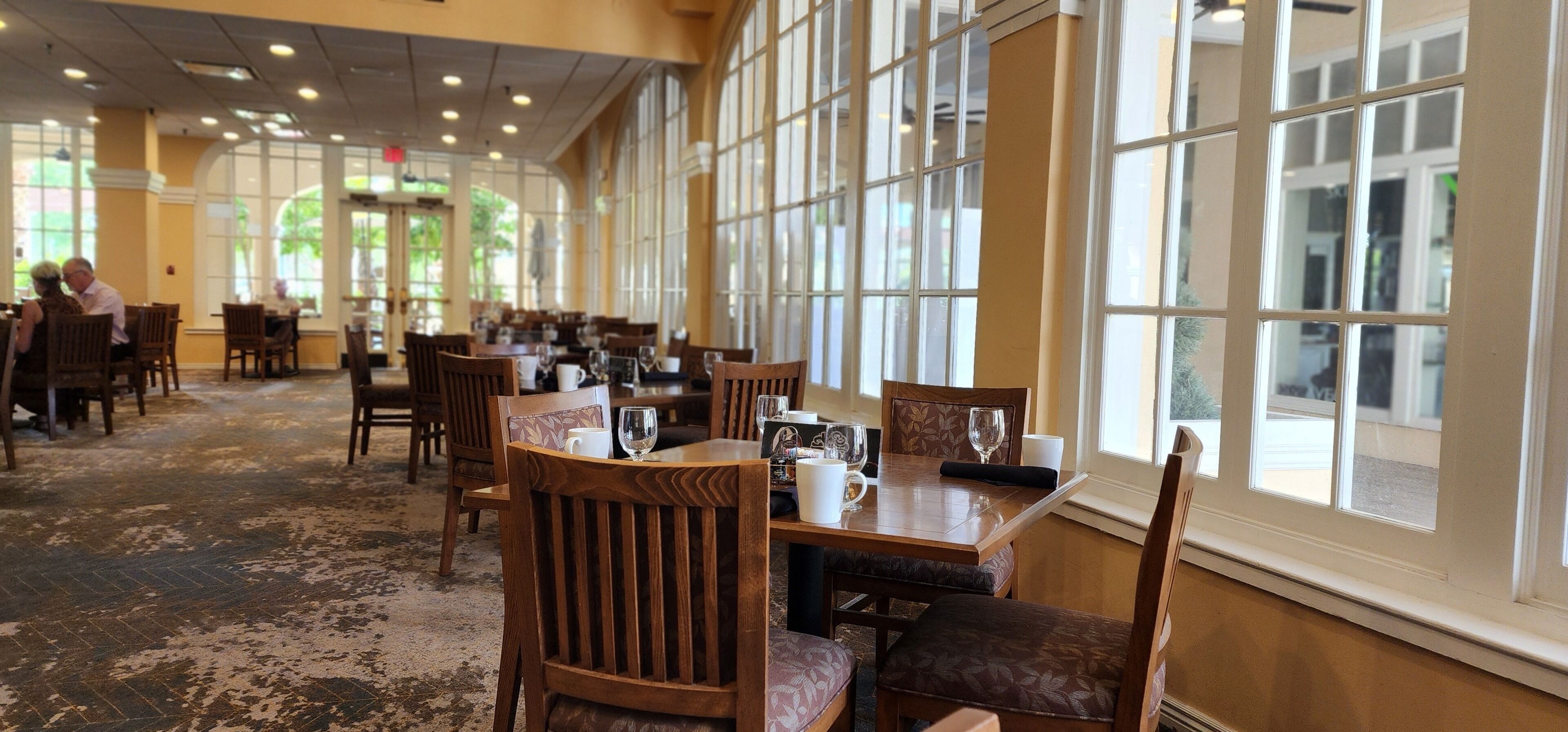 Un comedor amplio con ventanas grandes, mesas y sillas de madera.