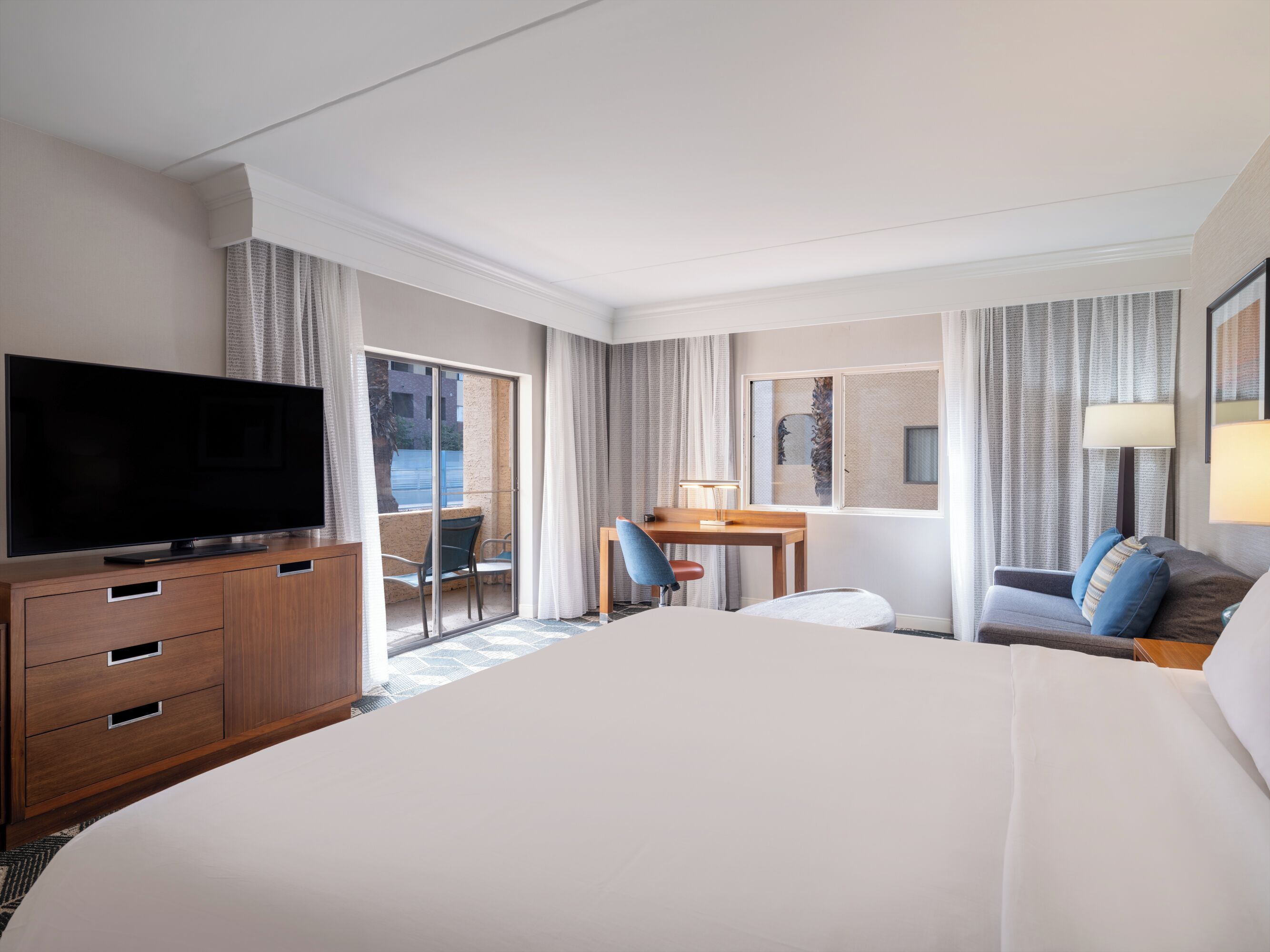 Habitación de hotel con una cama grande, un televisor de pantalla plana, un escritorio con silla, un sofá y una ventana con cortinas.