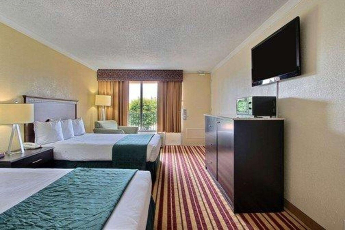 A hotel room with two beds, a television, a desk, and a window with curtains.