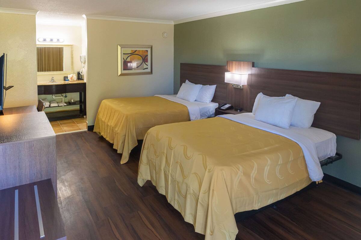 A hotel room with two beds, a desk, a mirror, and a bathroom.