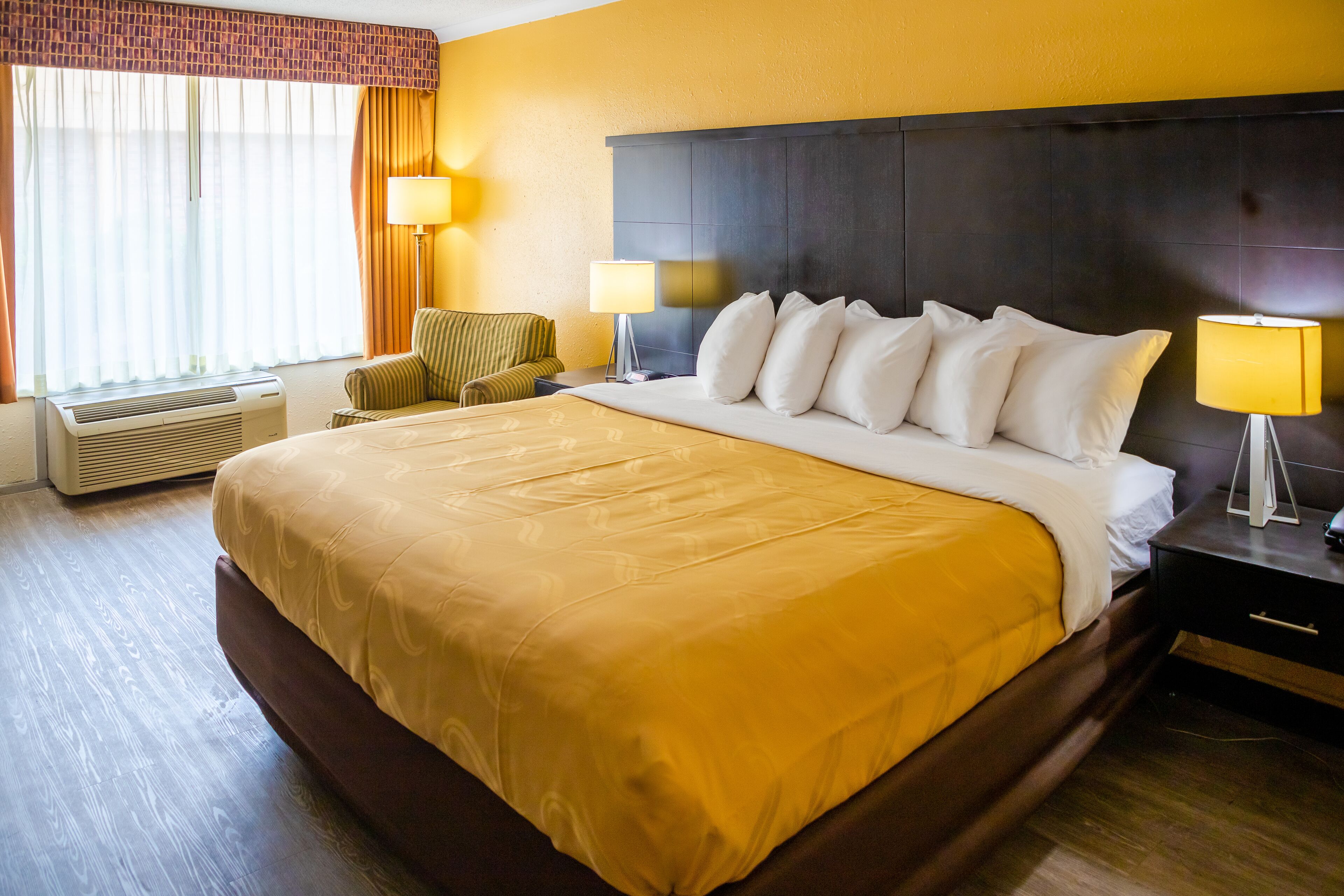 Una habitación de hotel con una cama grande, dos lámparas de noche, una silla, un escritorio y una ventana con cortinas.