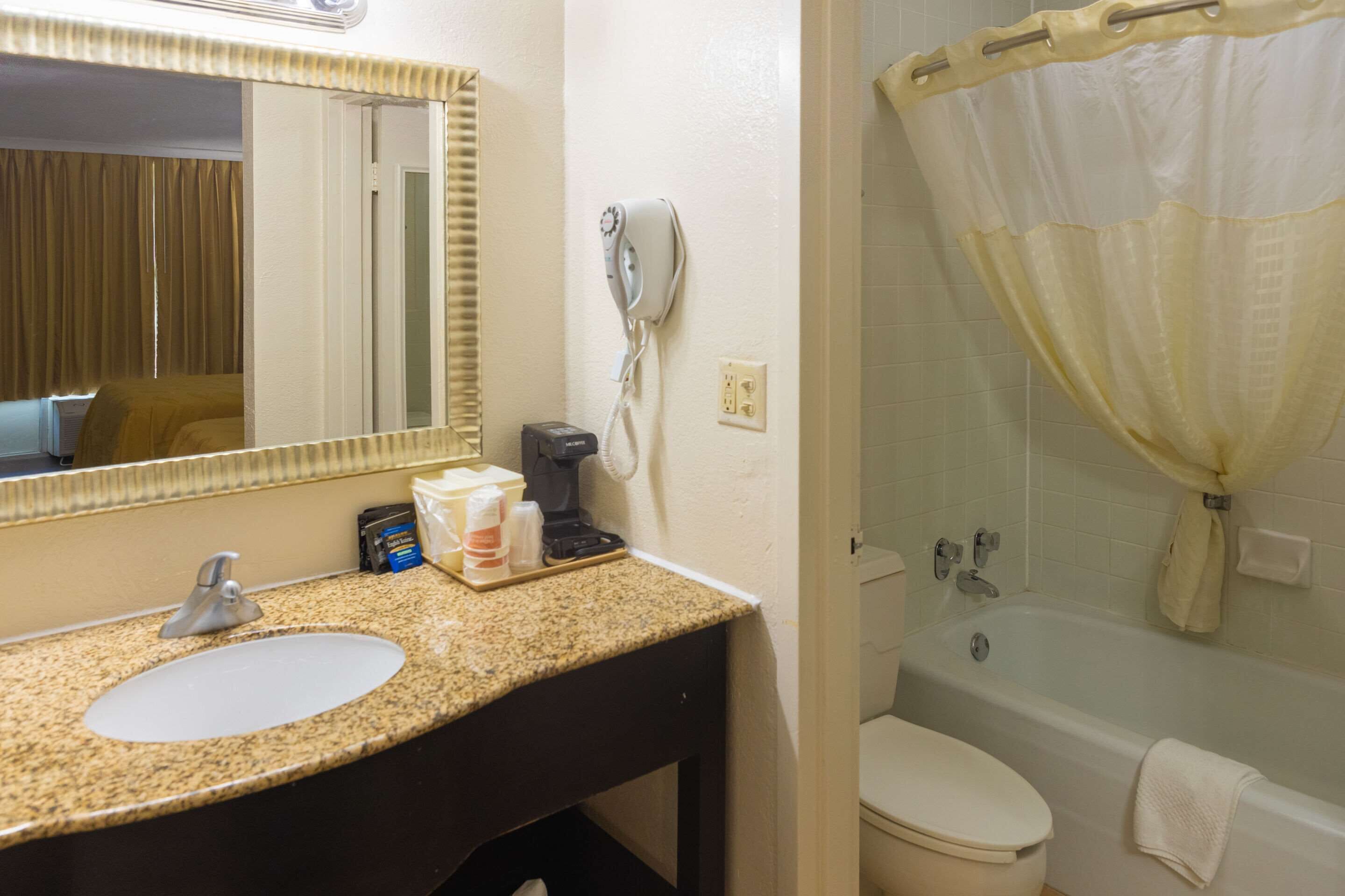 A bathroom with a sink, mirror, hairdryer, and a bathtub with a shower curtain.