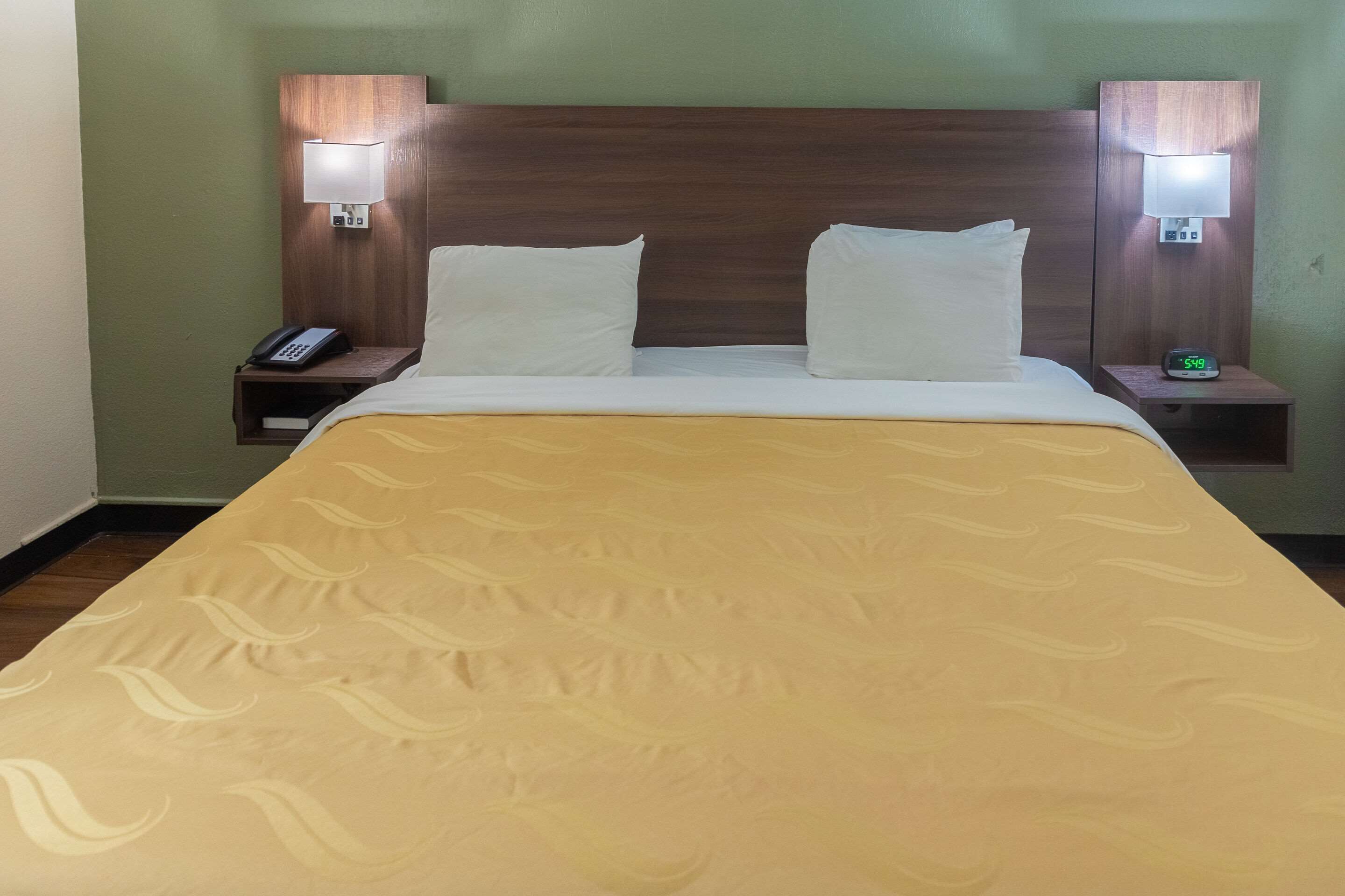 A hotel room with a bed, two bedside tables, a nightstand, a phone, and a digital clock.