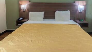 A hotel room with a bed, two bedside tables, a nightstand, a phone, and a digital clock.
