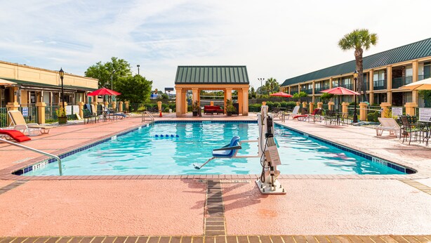 Une piscine entourée de chaises longues et de parasols, elle-même bordée de bâtiments dotés d’un toit végétalisé et d’un pavillon couvert situé au centre.
