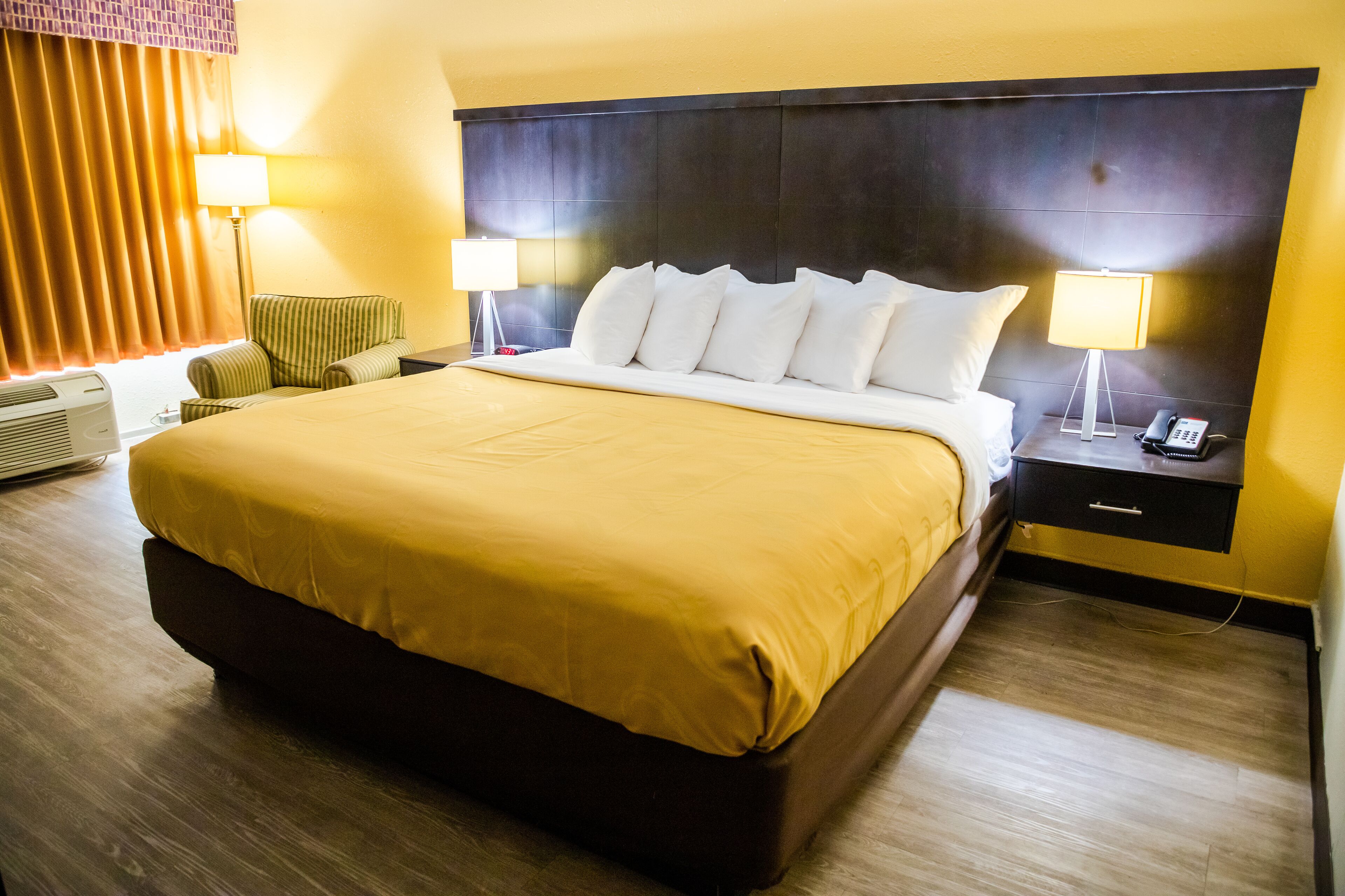 A hotel room with a large bed, two bedside tables with lamps, a chair, and a nightstand with a phone.