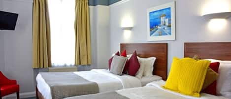 Quarto de hotel com duas camas, uma cadeira vermelha, um quadro na parede e uma janela com cortinas.