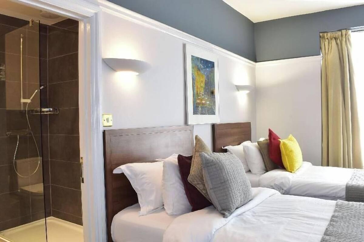Une chambre d’hôtel avec une douche, deux lits, une tête de lit et un tableau au mur.