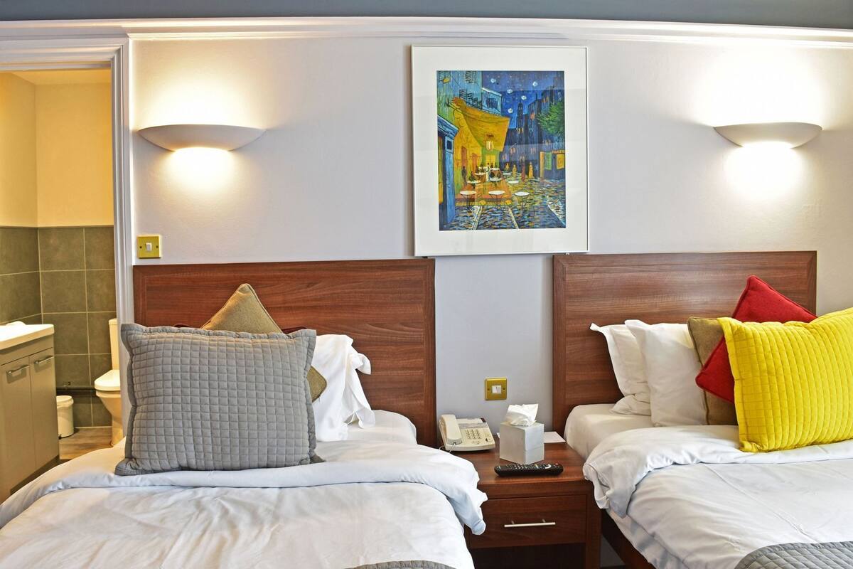 Une chambre d’hôtel avec deux lits, un tableau au mur et une salle de bain visible sur la gauche.
