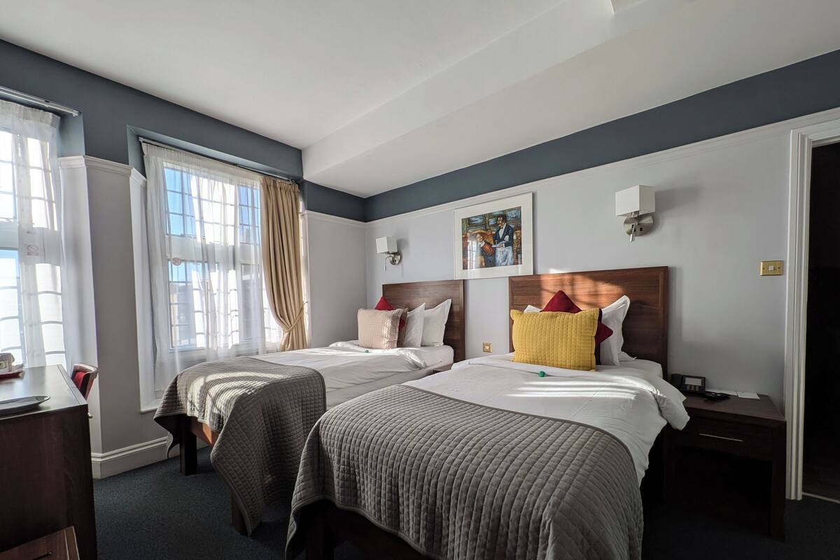 Une chambre d’hôtel avec deux lits, un bureau et une fenêtre avec des rideaux.