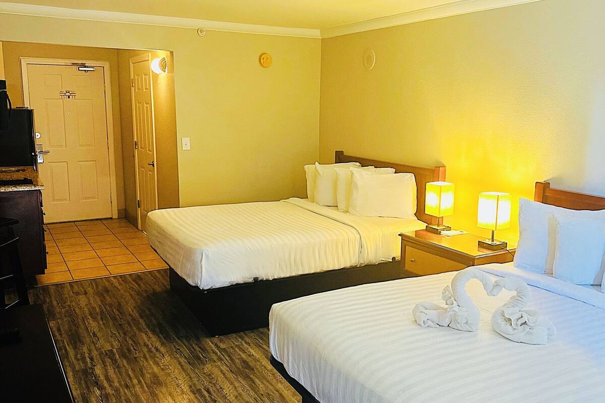 A hotel room with two beds, a desk, a chair, and a door.