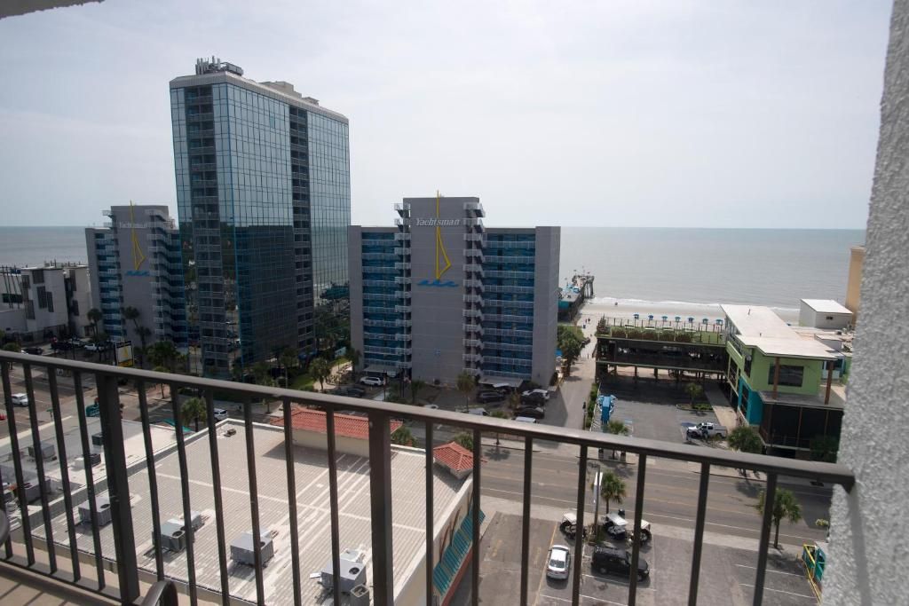 A high-rise building with a modern glass facade, a marina with boats, and a clear view of the sea.