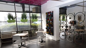 Un interior moderno con amplios ventanales, una instalación artística con una rueda de bicicleta en la pared, y un muro cubierto de plantas verdes.