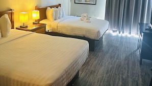Habitación de hotel con dos camas, una mesita de noche con lámparas, un cuadro enmarcado en la pared y un ventanal con cortinas.