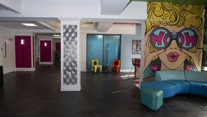 Un vestíbulo moderno con un sofá azul, sillas coloridas y un gran mural de arte pop.