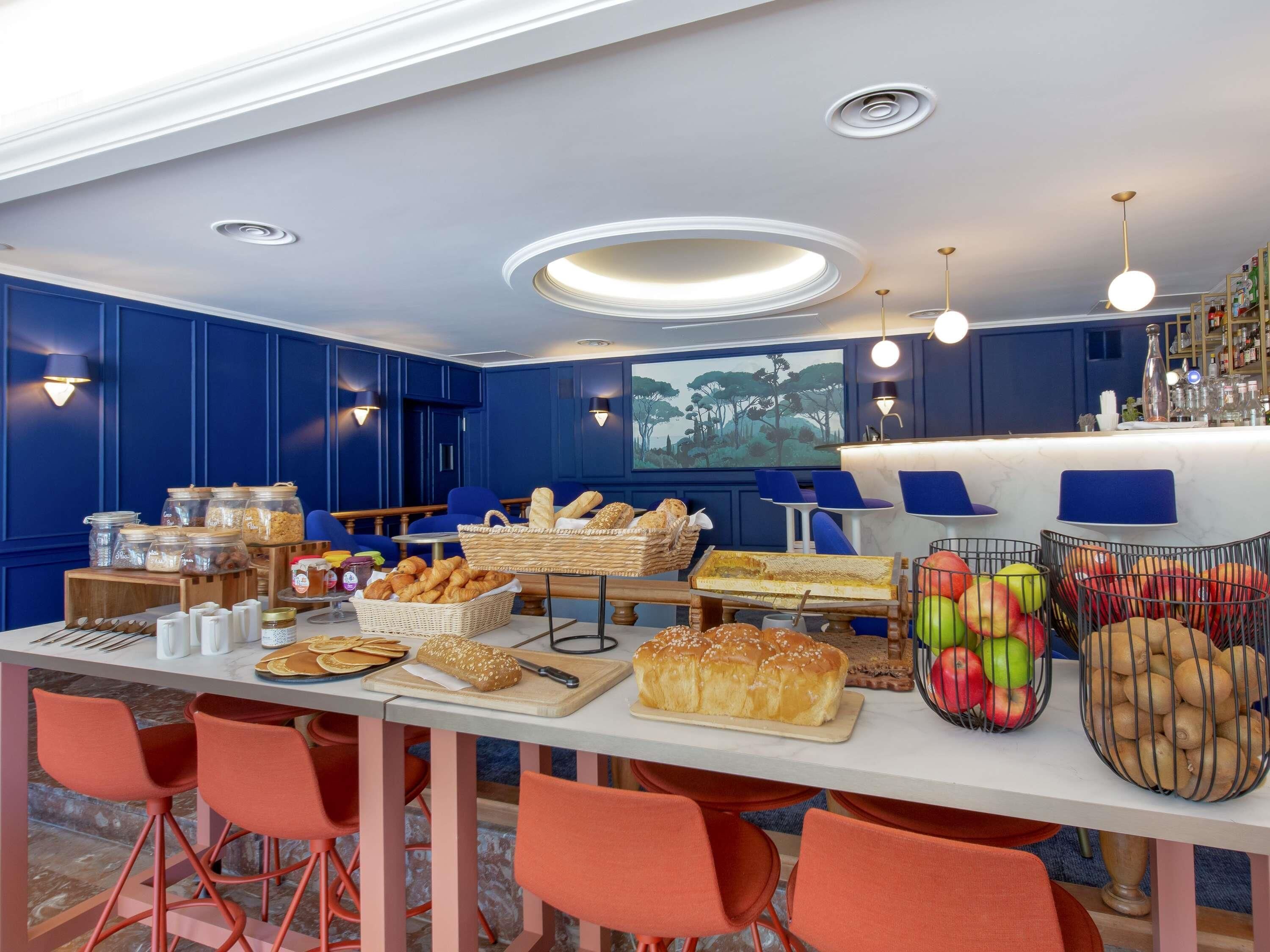 A bar area with seating, a buffet with bread and pastries, and a fruit display.