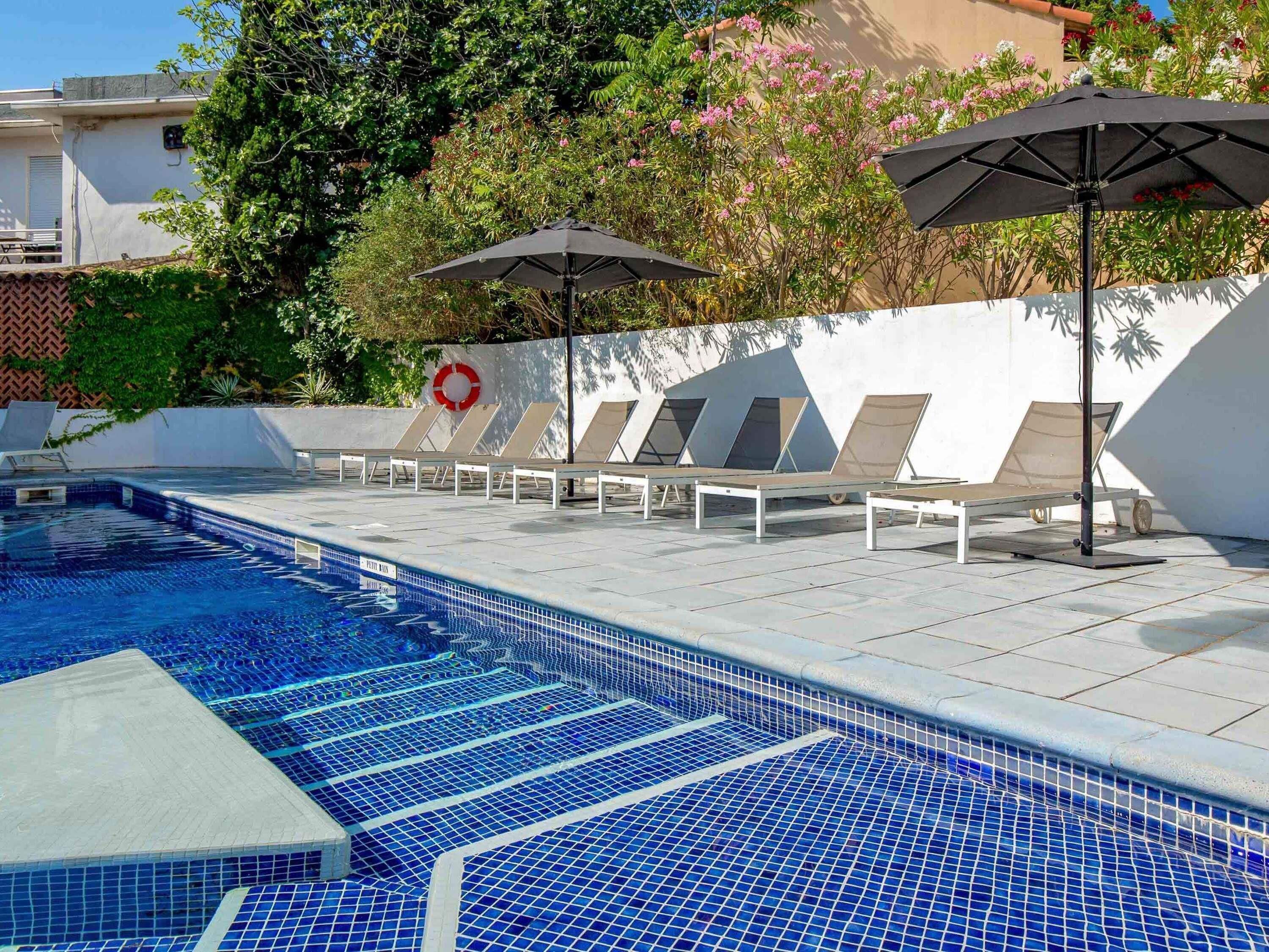 Una piscina con suelo de baldosas, tumbonas y sombrillas.