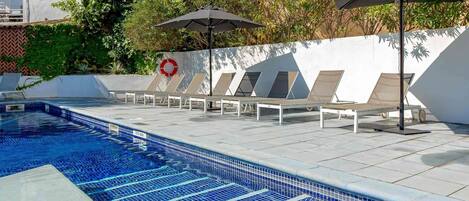 Una piscina con suelo de baldosas, tumbonas y sombrillas.