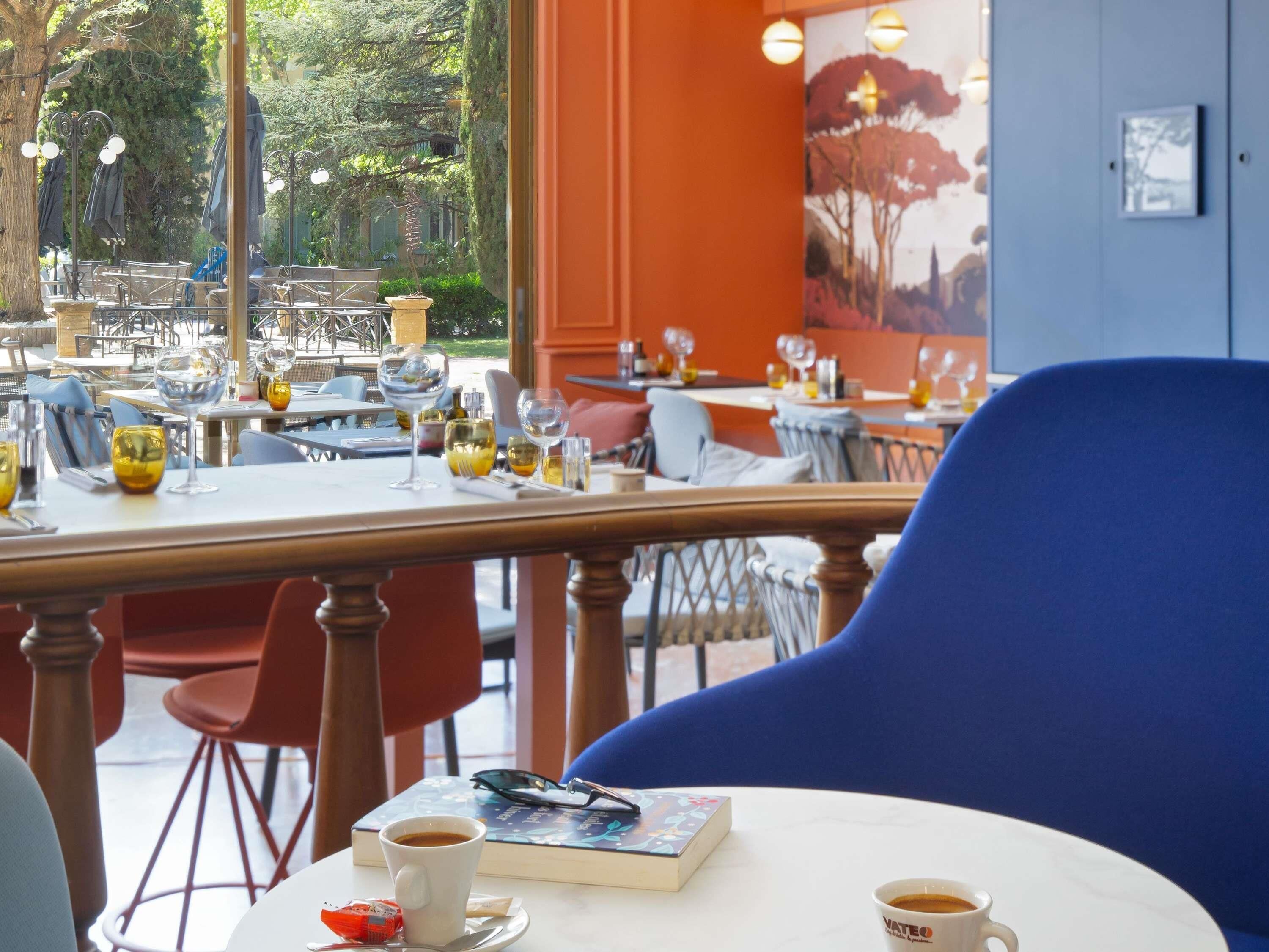 Um café ao ar livre com mesas e cadeiras, algumas com bebidas e livros.