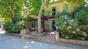 Ein traditionelles, zweistöckiges Gebäude mit einem Balkon, umgeben von üppiger Vegetation und blühenden Pflanzen.
