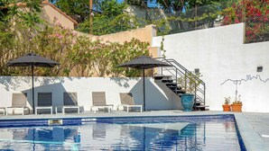 Ein Schwimmbecken mit Liegestühlen und Sonnenschirmen, eine Treppe und eine Wand mit einer Linienzeichnung.