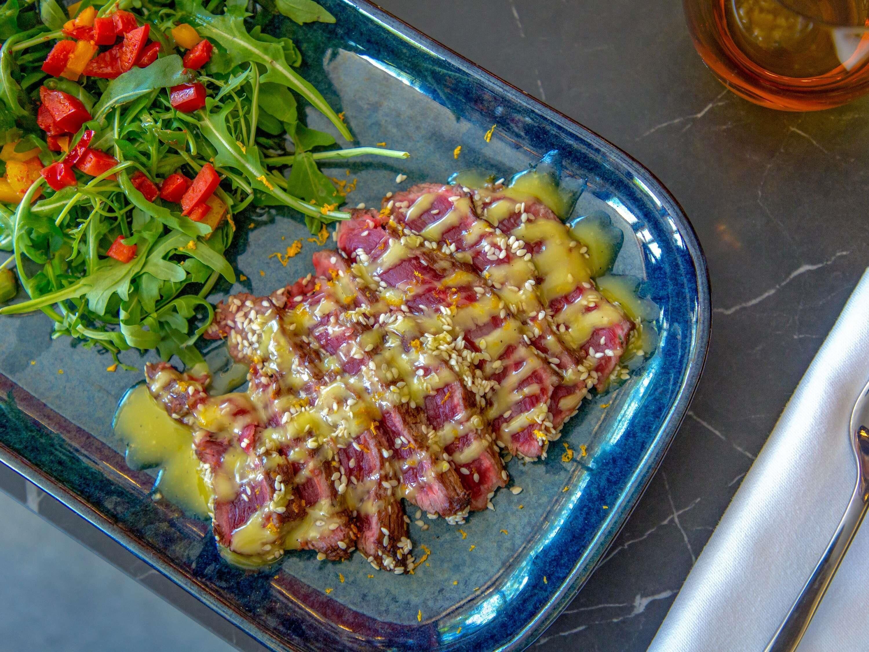 A plate of sliced meat with sesame seeds and a side salad.