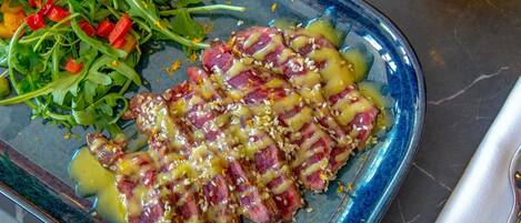 A plate of sliced meat with sesame seeds and a side salad.